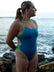 Model Kim standing on the beach gazing into the distance, wearing the JAYD Swimwear Ibiza one piece in nordic blue with contrasting moss green hip cut-outs and shoulder straps.