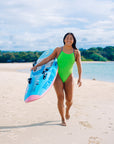 Surf life saving athlete Sara walking down a beach wearing the Splice x Storm Ibiza one piece swimsuit carrying her ski board on the way to a training session.