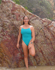 JAYD Swimwear Atlantic x Lilac Haze Ibiza One Piece contrasting against a rocky beachside background, worn by ski paddler Jenaya Massie.