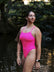 Athlete Jenaya standing in a river with a green forest behind her, wearing the JAYD Isla one piece in pink sorbet.