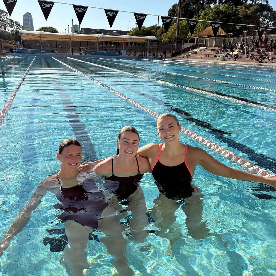 Three girls wearing JAYD Swimwear’s chlorine-resistant performance one pieces in a chlorine pool, showcasing fabric engineered to resist fading, maintain elasticity and support high-intensity swim training.