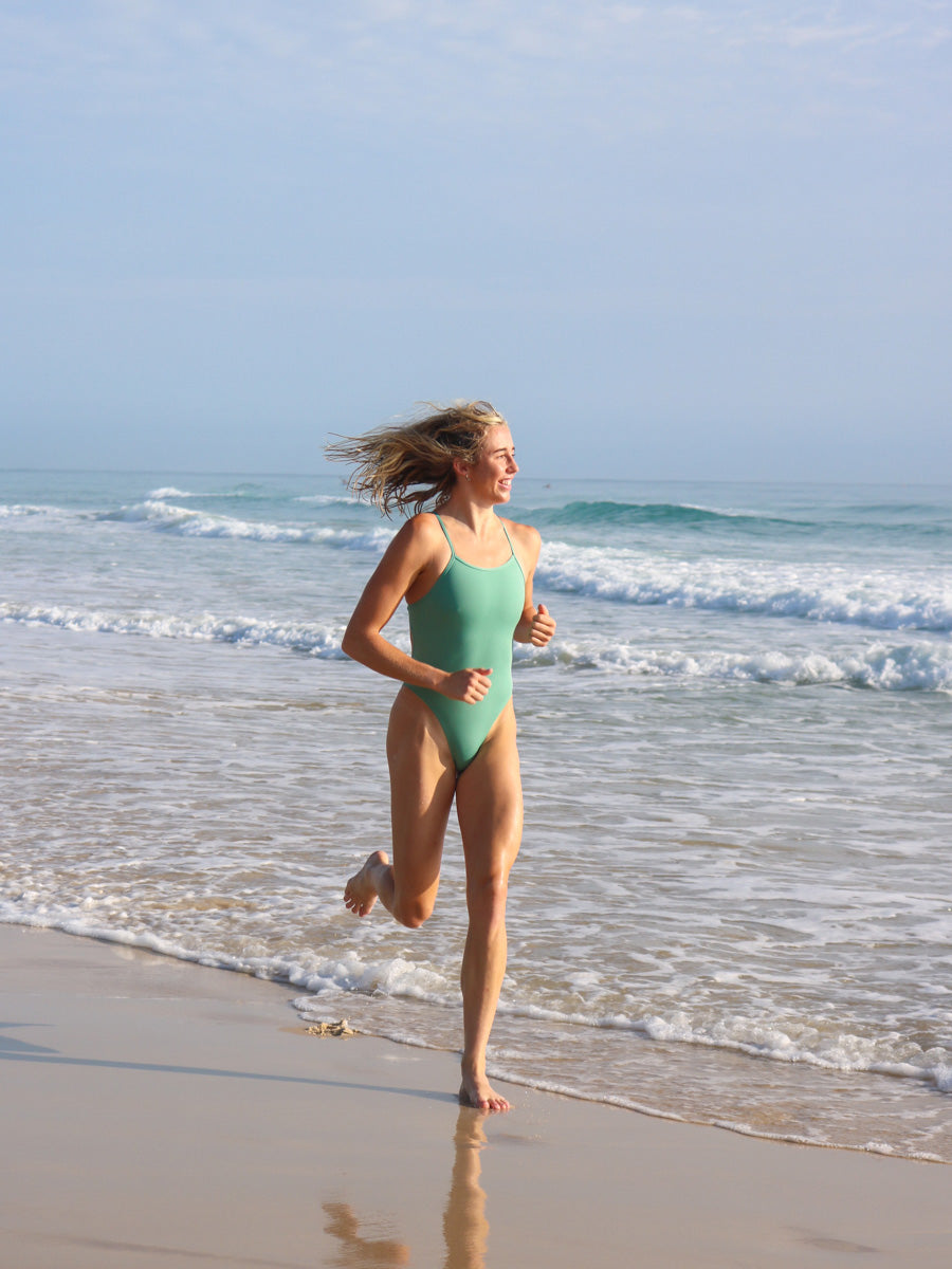 Running down the beach in our cheeky one piece called Zimmy. This colour is called Matcha and is designed by JAYD Swimwear