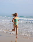 Running down the beach in our cheeky one piece called Zimmy. This colour is called Matcha and is designed by JAYD Swimwear