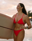Ski paddler Jenaya Massie carrying her surfboard along the beach in the JAYD Connie Ruby bottoms.