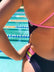 Close-up of Ella Ramsay wearing a dark acai purple JAYD Swimwear Lennox one-piece swimsuit with bright pink fairy floss and multicolor striped side straps, standing by a swimming pool.
