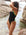 Distance swimmer, Madi Armstrong, wearing a black JAYD Swimwear one piece Lennox swimsuit with Splice green straps standing near rocky water.