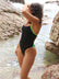 Distance swimmer, Madi Armstrong, wearing a black JAYD Swimwear one piece Lennox swimsuit with Splice green straps standing near rocky water.