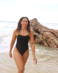 Distance swimmer, Madi Armstrong, wearing a black JAYD Swimwear one piece Lennox swimsuit with Splice green straps walking along a beach.