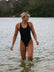 Front view of an athletic woman in a black JAYD Swimwear Levanto one piece swimsuit, wading in the water on a beach at sunrise.