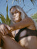 Woman in a brown JAYD Swimwear bikini top, Nalu in Cacao, sitting outdoors with plants and blue sky in the background