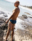 Side profile of Tanner wearing the Ramshark men’s swim bottom in Cove by JAYD Swimwear. Designed for freedom of movement and built from chlorine-resistant fabric.