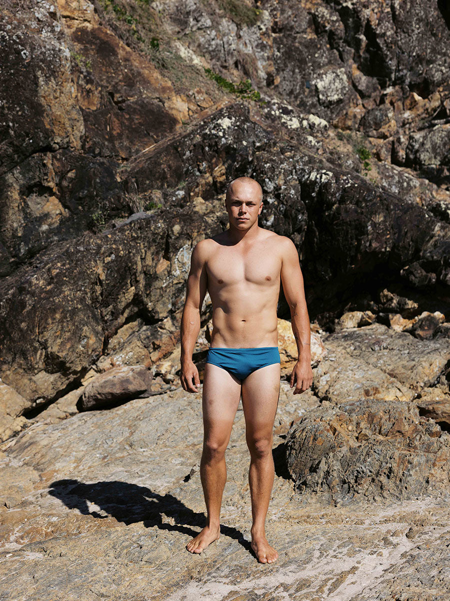 Ocean athlete Tanner wears the chlorine-resistant Ramshark men’s swim bottom in Cove by JAYD Swimwear. Front view highlighting the sleek, performance fit designed for movement.