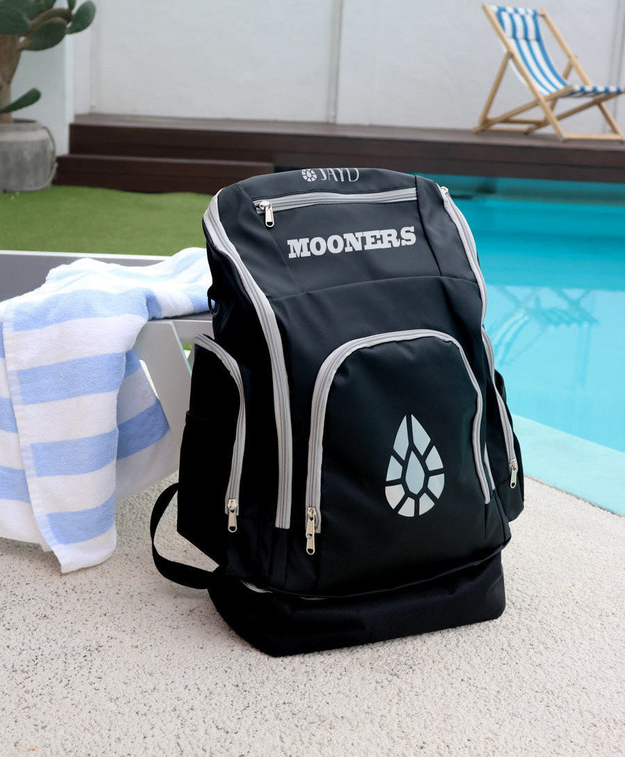 Black backpack with 'MOONERS' branding by a poolside