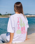 Back view of a model in JAYD Swimwear's white oversized tee, printed with a playful pink JAYD word mark, cactus, and cowgirl boots graphic.
