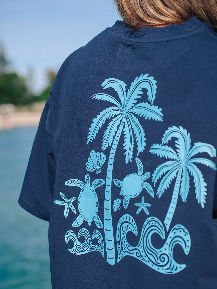 Back view of a model wearing JAYD Swimwear's navy oversized tee with a light blue turtle and palm tree graphic, styled for a post-swim, beach lifestyle.