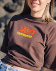 Close-up of a woman wearing a brown JAYD Swimwear oversized tee with a retro orange and yellow JAYD Swimwear logo print on the front.
