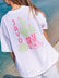 Woman wearing a white JAYD Swimwear oversized boxy tee with a pink cowgirl boots and cactus graphic print on the back, styled at the beach.