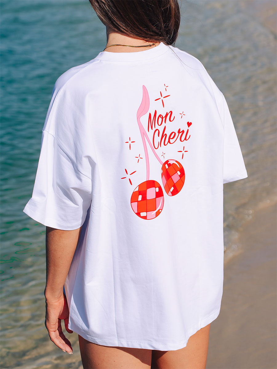 Back view of a model in JAYD Swimwear's white oversized tee, printed with a red disco-ball cherry graphic and Mon Cheri text.
