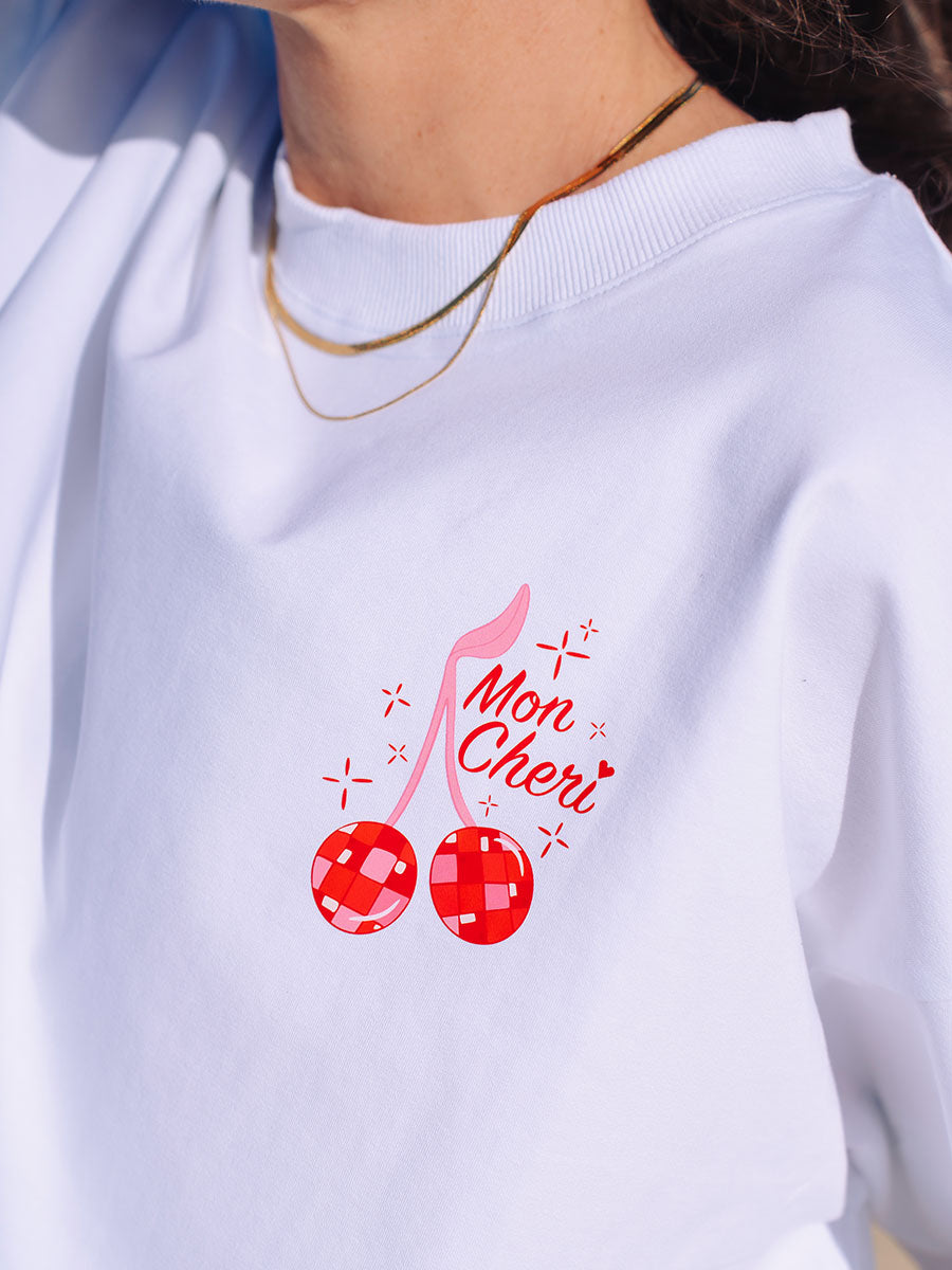 JAYD Swimwear white boxy fit t-shirt featuring a red sparkly cherry design and Mon Cheri script lettering on the back.
