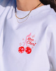 JAYD Swimwear white boxy fit t-shirt featuring a red sparkly cherry design and Mon Cheri script lettering on the back.
