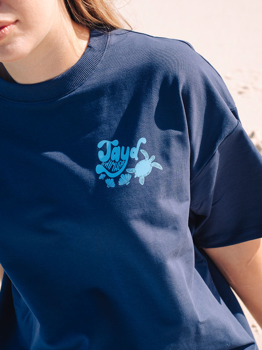 JAYD Swimwear navy boxy fit t-shirt featuring a blue ocean-inspired back print, styled with denim jeans for an oversized, laid-back beach look.