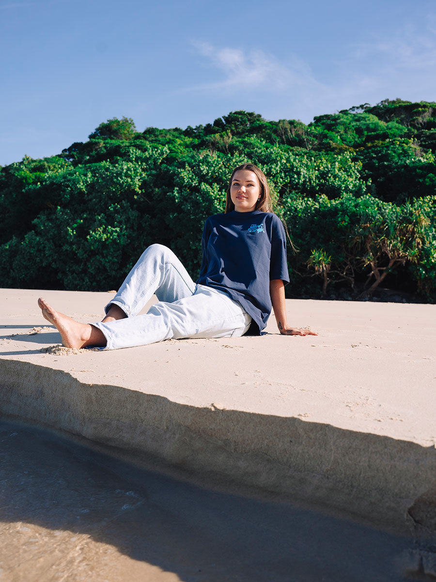 Navy oversized JAYD Swimwear t-shirt with a light blue coastal graphic on the back, an everyday boxy fit tee for lounging, beach days, or after a swim.