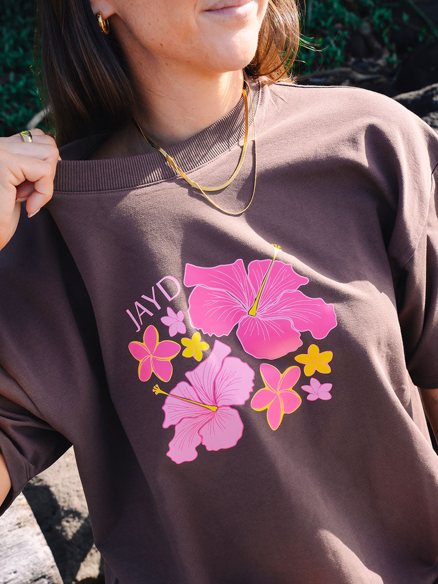 Front view of a model wearing JAYD Swimwear's brown oversized tee, printed with a tropical pink and yellow hibiscus flower graphic.