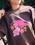 Front view of a model wearing JAYD Swimwear's brown oversized tee, printed with a tropical pink and yellow hibiscus flower graphic.