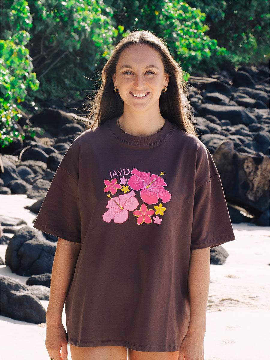Brown oversized JAYD Swimwear t-shirt with a pink hibiscus floral front print, an everyday boxy fit tee for beach days and tropical getaways.
