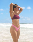 Front view of a female swimmer in a JAYD Swimwear Torquay bikini top in Sangria and pink bikini bottoms, standing on a beach.
