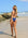 Back view of a female swimmer in a navy blue JAYD Swimwear athletic Zambia one piece swimsuit, standing on a beach with ocean and rocks in the background