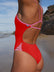 Close side view of a female swimmer wearing a Ruby red JAYD Swimwear one piece swimsuit with pink Fairy Floss straps, standing on a beach.