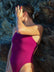 Side view of model leaning against a rock wearing JAYD Swimwear athletic tie-back one piece Riva in Sangria.