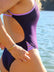 Close side view of model on beach wearing JAYD Swimwear athletic one piece swimsuit Zambia in Acai.