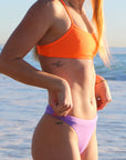 Side view of model on a beach wearing JAYD Swimwear athletic bikini top Torquay in Neon Orange.