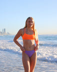 Front view of model on a beach wearing JAYD Swimwear athletic bikini top Torquay in Neon Orange.