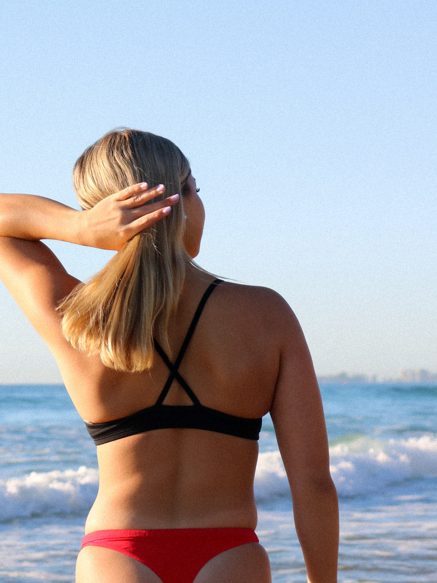 Back view of model on a beach wearing JAYD Swimwear athletic bikini top Torquay in Black.