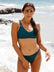 Female swimmer in Cove Tazzie JAYD Swimwear bikini top standing on a beach with ocean waves in the background.