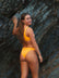 Back view Australian triathlete, Charlotte Derbyshire, wearing a JAYD Swimwear Cali bikini bottom in Sunshine Yellow against a rocky background.