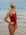 Female athlete in a JAYD Swimwear Finley swimsuit in Cinnamon, standing on a beach with ocean in the background