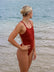 Female athlete in a JAYD Swimwear Finley swimsuit in Cinnamon, standing on a beach with ocean in the background