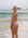 Back view of a female athlete in a JAYD Swimwear Torquay bikini top in lilac haze, standing on a beach with waves in the background.
