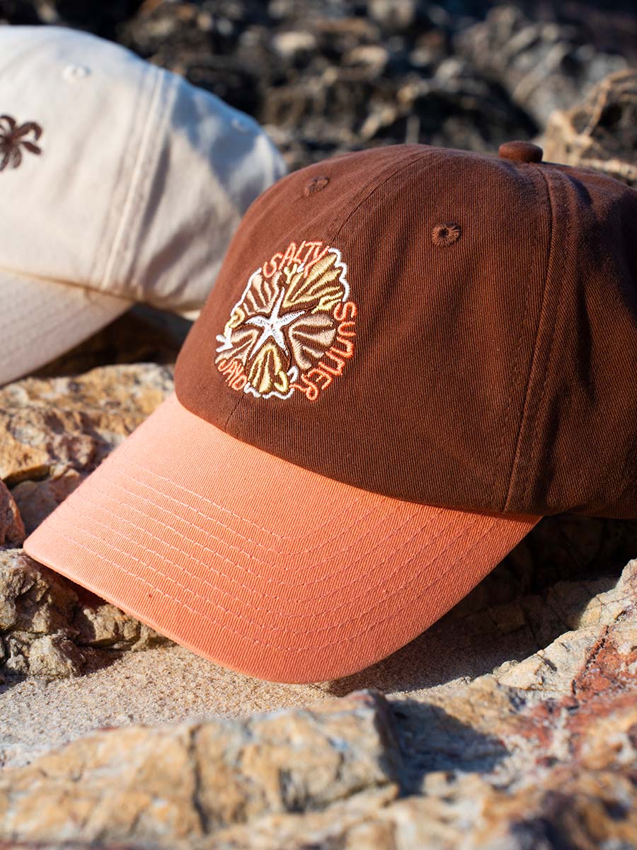 JAYD Swimwear Brown & Apricot Baseball Cap sitting on a rock.