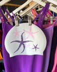 JAYD swim cap Starfish, hanging on a rack with purple and pink JAYD one piece swimsuits.