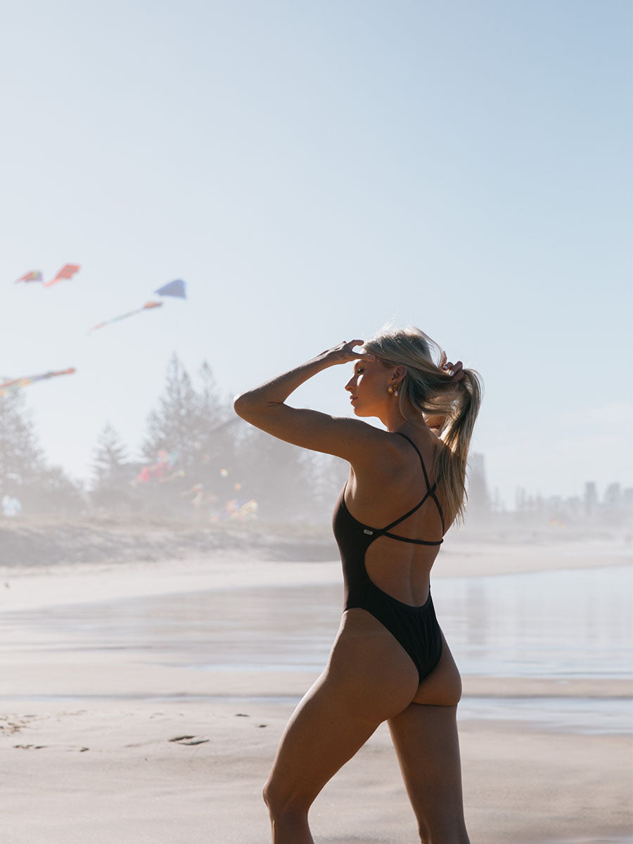 Woman in a Cacao brown JAYD chlorine resistant swimsuit on a beach with kites in the background