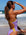 Athlete Molly wearing the Lilac Haze JAYD one piece in Lennox, with contrasting daffodile yellow straps and hip cut-outs, standing on a beach looking into the distance with ocean waves in the background.