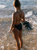 Brodee wears the Tallow One Piece in Carbon grey, walking along a beach with waves.