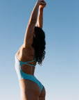 Madi wearing the Tallow One Piece swimsuit in MYKONOS blue against a clear blue sky.