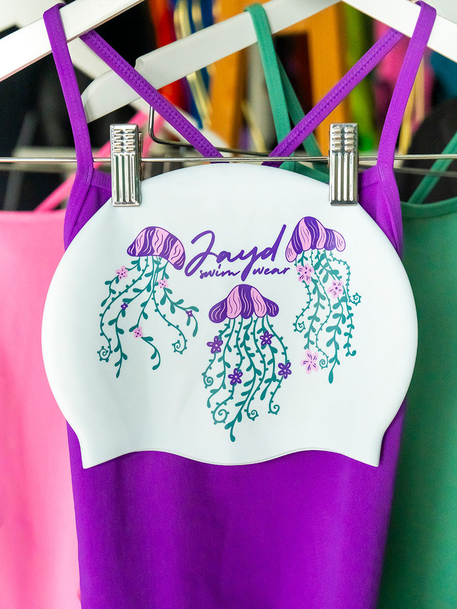 JAYD Swimwear white swim cap featuring three floral jellyfish illustrations, complimented by matching swimsuits.