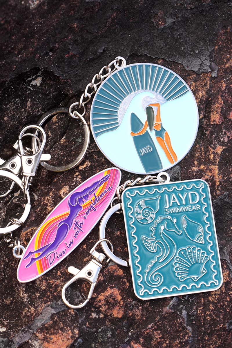 Various colourful JAYD Swimwear keychains sitting on a rock